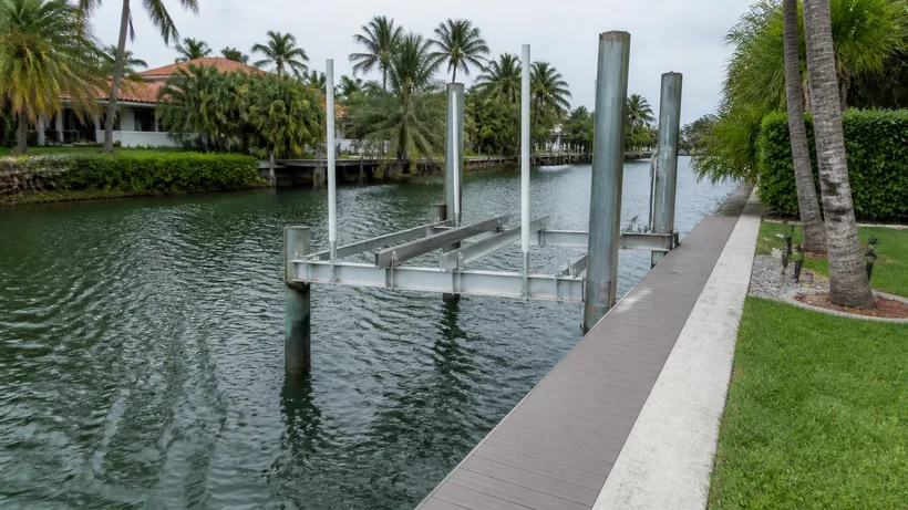 Empty boat lift on piles beside a canal seawall with a narrow deck platform along the cap