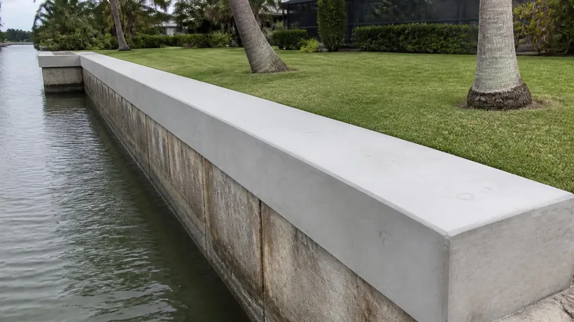 Freshly poured concrete cap with crisp formed edges sitting on the older stained wall face below